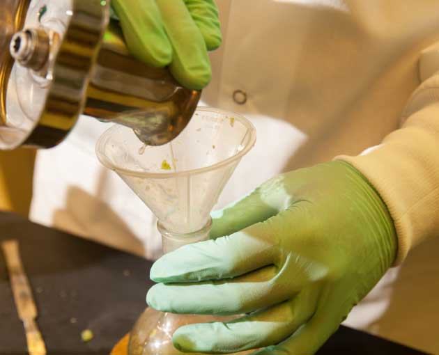 Gloves hands pouring a liquid into a glass container