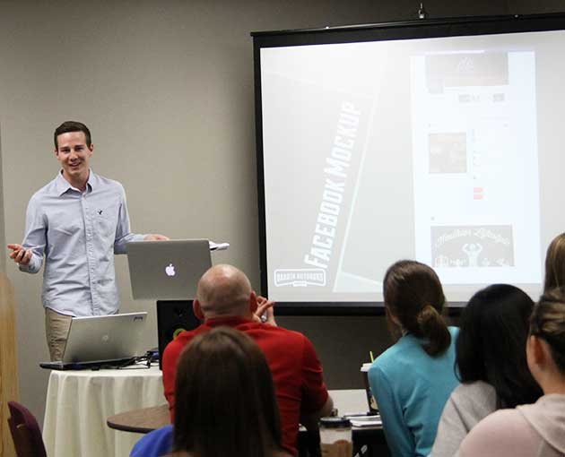 A smiling professor is shown at the front of a classroom