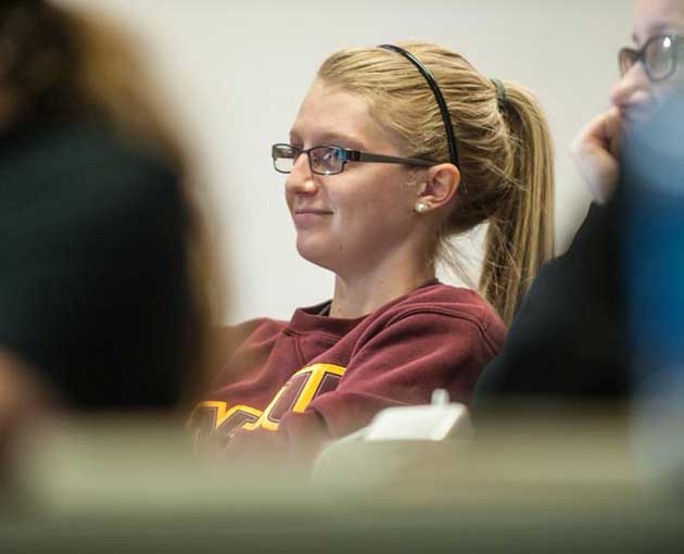 A student with long hair, ponytail and black glasses attends in class