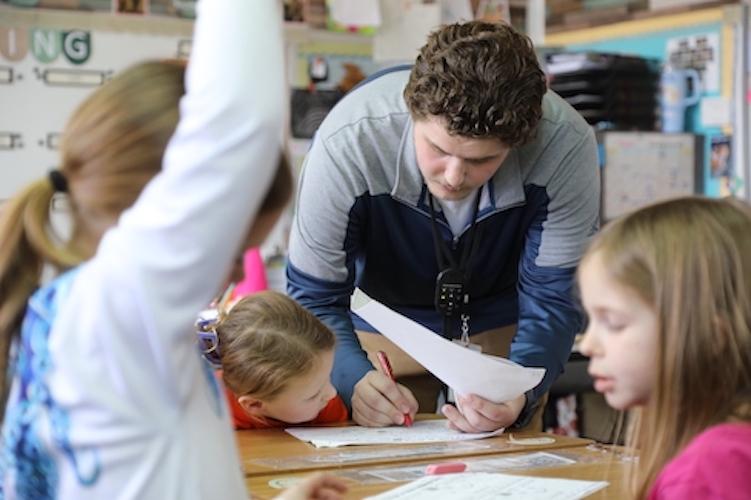 Male student teacher helping children at a desk