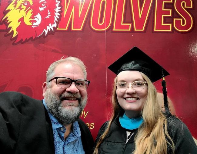 Graduate standing with her father in front of an NSU Wolves display